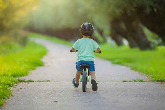 Robin on his balance bike, seen from behind, on a sunny park path